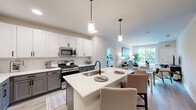 This well-appointed 2-bedroom, 2-bathroom residence at 250 McHenry Road in Buffalo Grove, IL offers a thoughtfully designed single-floor layout with modern finishes and an open, airy feel. The combined kitchen and dining area serves as the heart of the home, showcasing two-tone cabinetry with white uppers and gray lowers, stainless steel appliances, a subway tile backsplash, and a large central island with a undermount sink and pendant lighting — ideal for both meal prep and casual dining. The open-concept layout flows seamlessly into the living room, which is bathed in natural light from large sliding glass doors that open onto a private balcony with outdoor views of lush greenery. Both bedrooms feature plush carpeting, generous windows with outdoor views, and ample closet space. The primary bathroom is well-equipped with a dual-sink vanity featuring gray cabinetry, a walk-in shower, and a dedicated walk-in closet. The second bathroom mirrors the same refined aesthetic with stylish fixtures and storage. Light wood-style flooring runs throughout the main living areas, complementing the neutral, contemporary color palette. Additional conveniences include an in-unit laundry area, a utility room, and multiple hallway closets, ensuring practical storage throughout.