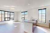 Located at 2950 Arkins Ct in Denver's RiNo neighborhood, this modern 3-bedroom, 2-bathroom residence offers a thoughtfully designed single-level layout with clean, contemporary finishes throughout. The open-concept kitchen and living area serves as the heart of the home, featuring light hardwood-style flooring, recessed lighting, and a striking central island with a sleek gray countertop and undermount sink. The kitchen is equipped with warm wood cabinetry, stainless steel appliances including a refrigerator, range, and microwave, and is framed by large black-gridded windows that flood the space with natural light and offer urban views of the Denver skyline. The living area extends generously from the kitchen, benefiting from the same abundant natural light. The three bedrooms feature plush carpeting, ceiling fans, and oversized black-framed windows. The primary bedroom is a comfortable retreat with dual windows and ample space. A dedicated mudroom/closet area with built-in lower cubbies and wall hooks adds practical storage. The two bathrooms are finished with wood-tone vanities, white countertops, and light hardwood-style flooring — one with a glass-enclosed walk-in shower and one with a full tub-shower combo, both featuring clean white tile surrounds.