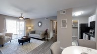 This 2-bedroom, 1-bathroom residence is thoughtfully arranged on a single floor, offering a comfortable and efficient layout. The open-concept living and dining area serves as the heart of the home, featuring warm wood-look hardwood flooring that extends throughout the space, creating a cohesive and modern aesthetic. Neutral gray-toned walls provide a versatile backdrop, complemented by white trim and ceilings that brighten the interior. The living area is generously proportioned, accommodating a full seating arrangement with ease, and benefits from natural light streaming in through large windows. A ceiling fan adds both style and practicality to the space. A partial wall divides the living area from the dining zone, adding architectural interest while maintaining an open flow. The dining area transitions smoothly into a well-organized kitchen, which features visible shelving and ample storage. A hallway leads to the two bedrooms, with closet access visible along the corridor. The overall ambiance is clean, welcoming, and move-in ready, with updated finishes that give the home a fresh, contemporary feel throughout.
