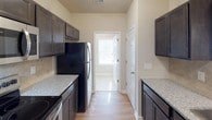 The Sunset is a thoughtfully designed single-floor residence that combines practical functionality with comfortable living. The kitchen serves as a central highlight, featuring dark espresso-toned cabinetry, granite-style countertops, and a full suite of stainless steel appliances including a refrigerator, electric range, and built-in microwave. Light wood-style flooring runs through the kitchen and dining areas, complementing the warm, neutral color palette maintained throughout the home. The galley-style kitchen layout maximizes efficiency, with cabinetry lining both sides and a window at the far end inviting natural light into the space. The dining area features a decorative chandelier and direct access to the entry, creating a welcoming first impression. The bedrooms are carpeted for comfort and each equipped with ceiling fans, offering a calm and restful atmosphere. One bedroom benefits from a window with blinds, allowing for both natural light and privacy. The bathroom is well-appointed with dark wood vanity cabinetry, a wide mirror, dual towel rings, and a full soaking tub with a shower surround. Clean tile flooring and bright wall sconces complete the space. Overall, The Sunset presents a cohesive, move-in-ready environment with consistent finishes and a neutral aesthetic throughout.
