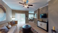 This single-floor residence offers a thoughtfully designed layout that balances comfort and functionality. The living room serves as the heart of the home, featuring warm carpeting, crown molding, a ceiling fan with light fixture, and sliding glass doors with vertical blinds that invite natural light and outdoor views. The space flows seamlessly into a dining nook enclosed by large windows, filling the area with abundant natural light and garden views.

The kitchen is equipped with light wood cabinetry, white appliances including an electric range and dishwasher, white countertops, a stainless steel double sink, and hardwood-style flooring — offering both practicality and a clean aesthetic.

Two well-sized bedrooms provide comfortable retreats, each carpeted and featuring windows with views of the surrounding greenery. The primary bedroom benefits from a bay window configuration that enhances its sense of space and light, while the second bedroom includes its own window with outdoor views.

Both bathrooms are finished consistently, featuring light wood vanity cabinetry, white countertops, tile flooring, a tub-shower combination with a curtain, and overhead cabinetry for additional storage. The warm, neutral color palette used throughout the residence creates a cohesive and inviting atmosphere from room to room.