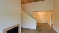This two-floor home offers a straightforward and functional layout designed for comfortable everyday living. The main level centers around a carpeted living area that exudes a warm, understated ambiance. A tiled fireplace with a classic black surround serves as a natural focal point, adding character and a cozy element to the space. An open staircase with clean white walls rises prominently from the living area, providing easy access to the upper floor while contributing to the open feel of the main level. Adjacent to the living space is a defined dining area, separated subtly by a partial wall and illuminated by a simple pendant light fixture that hangs from the ceiling, lending the space a touch of warmth. The consistent warm-toned walls and neutral carpet throughout create a cohesive and inviting atmosphere. Recessed lighting on the upper portion of the staircase wall adds a modern touch and ensures the space is well-lit. Overall, this home presents a clean, move-in ready environment with timeless finishes suited for a range of interior styles.