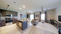 This two-story home is designed with a clean, contemporary aesthetic that emphasizes open living on the main floor. The entry foyer welcomes visitors with light wood-look flooring and a well-appointed staircase featuring white balusters and carpeted treads, providing a clear view down a hallway that connects to the main living areas.

The heart of the home is an expansive open-concept space that seamlessly integrates the kitchen, dining area, and living room. The kitchen is outfitted with dark, wood-toned cabinetry, stainless steel appliances, and a central island topped with granite countertops that doubles as a breakfast bar with white bar seating. Track lighting overhead highlights the workspace efficiently.

The dining area accommodates a full-sized table and flows naturally toward sliding glass doors that invite natural light into the space. The living room, positioned adjacent, benefits from multiple windows dressed with patterned drapes and is served by a ceiling fan. Recessed lighting throughout the main level ensures consistent, even illumination. The light flooring unifies the open layout, creating a bright and cohesive atmosphere throughout the first floor.