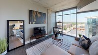 Located at 227 W Michigan Ave in the heart of downtown Kalamazoo, this contemporary urban residence blends industrial character with modern sophistication. The space is defined by its exposed concrete ceilings and structural columns, which lend an authentic loft-style aesthetic throughout.

The open living area is a standout, anchored by expansive floor-to-ceiling windows that flood the room with natural light and offer sweeping views of the Kalamazoo cityscape. The living space comfortably accommodates a seating arrangement and media setup, with the raw concrete ceiling adding texture and architectural interest overhead.

The kitchen is well-appointed with crisp white shaker cabinetry, dark granite countertops, a warm subway tile backsplash with under-cabinet lighting, and a full suite of stainless steel appliances, including a range, microwave, and refrigerator. Wood-look flooring runs throughout, tying the spaces together cohesively.

The bedroom offers a calm retreat, featuring a walk-in closet, exposed concrete ceiling consistent with the rest of the unit, and warm ambient lighting. A console table with a round mirror adds functional style to the space.

The bathroom is finished with white cabinetry, dark granite countertops, a large vanity mirror, and wood-look flooring, maintaining the refined aesthetic found throughout the residence.