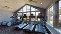 This fitness center in Horn Lake, Mississippi, is a thoughtfully designed facility that offers a comprehensive workout experience across a single level. The space is architecturally distinguished by soaring vaulted ceilings in the cardio area, where a dramatic floor-to-ceiling triangular window wall floods the room with natural light and provides open views of the surrounding landscape. Ceiling fans throughout help maintain a comfortable environment during workouts.

The cardio zone is well-appointed with multiple treadmills and elliptical trainers, each equipped with individual screens for entertainment during exercise. Patterned carpet tiles in neutral tones cover the floors throughout, providing both durability and visual warmth.

A dedicated strength training area features a well-rounded selection of equipment, including cable machines, a multi-functional weight machine, a Smith machine with a barbell and weight plates, an adjustable bench, and a full rack of dumbbells in varying weights. Full-length mirrors line the walls of the strength zone, enhancing the sense of space while allowing users to monitor their form.

The interior palette of cool gray walls is accented by bold navy blue feature walls, lending the space a modern, energetic atmosphere. Recessed lighting and natural light from additional side windows ensure the entire facility is bright and inviting throughout the day.