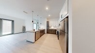 Located in Apollo Beach, Florida, this well-designed single-story residence offers two bedrooms and two bathrooms with a thoughtful, modern layout. The kitchen is a standout feature, showcasing a large central island with a quartz-style countertop, undermount sink, and stainless steel appliances including a refrigerator, range, and dishwasher. A two-tone cabinetry scheme pairs crisp white upper cabinets with rich dark wood lower cabinets, complemented by a classic subway tile backsplash and sleek pendant lighting. Light wood-style flooring runs throughout the main living areas, enhancing the bright, open ambiance. Each bedroom is carpeted and bathed in natural light through large windows fitted with blinds, and both include ceiling fans. Each bedroom is paired with its own walk-in closet, outfitted with wire shelving systems that maximize storage. The two bathrooms reflect a consistent modern aesthetic, featuring dark wood vanities with dual sinks, large mirrors, light wood-tone flooring, and tiled surrounds. The primary bathroom includes a glass-enclosed walk-in shower, while the second bathroom offers a tub-shower combination. The overall design is clean, contemporary, and functional throughout.