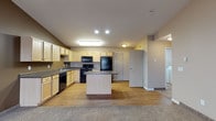 Located at 1710 13th Street SE in Minot, North Dakota, this single-floor unit offers a functional and comfortable layout designed for everyday living. The heart of the home is an open-concept kitchen equipped with light maple cabinetry, dark granite-style countertops, a full suite of black appliances including a refrigerator, electric range, built-in microwave, and dishwasher. A center island provides additional prep space and doubles as a casual dining area, while wood-style flooring ties the kitchen seamlessly into the adjacent living area. The living room is generously sized, featuring plush carpeting, a baseboard heating system, a wall-mounted air conditioning unit, and a sliding glass door that opens to a private balcony with outdoor views. The bedrooms are carpeted and well-lit by large windows that allow ample natural light, each also equipped with baseboard heating. The bathrooms include a full bath with a white soaking tub and shower combination, and a second bath with wood-style flooring, a vanity with granite-style countertops, and ample cabinetry. Neutral tones throughout create a clean, welcoming ambiance suited for a variety of interior styles.