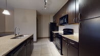 Located on Hayes Court in Beavercreek, Ohio, this single-floor residence offers a thoughtfully designed layout with a contemporary aesthetic throughout. The kitchen serves as a focal point of the unit, showcasing rich dark espresso cabinetry that extends to the ceiling, providing generous storage capacity. Light granite-style countertops contrast the dark finishes, while a central island features an integrated sink, a built-in wine rack below, and pendant lighting overhead. Track lighting illuminates the space, and black appliances — including a refrigerator, range, and built-in microwave — complete the kitchen's cohesive look. Large-format tile flooring runs through the kitchen and wet areas, transitioning to plush carpet in the living and sleeping areas. The living room is generously proportioned, finished in neutral tones, and opens to a private balcony through a sliding glass door, allowing natural light to fill the space. Bedrooms feature carpeted floors, ceiling fans, and windows that bring in additional natural light. The bathrooms are finished with tiled flooring, dark vanity cabinetry, well-lit mirrors, and a soaking tub with shower combination. A spacious walk-in closet with multi-rod storage provides practical organization. The overall ambiance is modern and neutral, offering a clean and functional living environment.