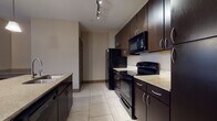 Located on Hayes Court in Beavercreek, Ohio, this single-floor residence offers a thoughtfully designed layout with a contemporary aesthetic throughout. The kitchen serves as a focal point of the unit, showcasing rich dark espresso cabinetry that extends to the ceiling, providing generous storage capacity. Light granite-style countertops contrast the dark finishes, while a central island features an integrated sink, a built-in wine rack below, and pendant lighting overhead. Track lighting illuminates the space, and black appliances — including a refrigerator, range, and built-in microwave — complete the kitchen's cohesive look. Large-format tile flooring runs through the kitchen and wet areas, transitioning to plush carpet in the living and sleeping areas. The living room is generously proportioned, finished in neutral tones, and opens to a private balcony through a sliding glass door, allowing natural light to fill the space. Bedrooms feature carpeted floors, ceiling fans, and windows that bring in additional natural light. The bathrooms are finished with tiled flooring, dark vanity cabinetry, well-lit mirrors, and a soaking tub with shower combination. A spacious walk-in closet with multi-rod storage provides practical organization. The overall ambiance is modern and neutral, offering a clean and functional living environment.