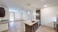 Located in Tomball, Texas, this well-appointed one-bedroom, one-bathroom unit offers a thoughtfully designed open-concept layout across a single floor. The kitchen serves as a central highlight, featuring a granite countertop island with a built-in sink and stylish pendant lighting overhead. Dark espresso cabinetry contrasts beautifully with the light granite surfaces, while stainless steel appliances — including a refrigerator, range, and microwave — complete the modern culinary space. Wood-style plank flooring flows throughout the main living areas, lending warmth and continuity to the space.

The living room is bright and airy, with a ceiling fan, natural light streaming through window blinds, and access to an outdoor area via a glass door. The bedroom offers plush carpeting, a ceiling fan, and a window that invites natural light. A walk-in closet provides organized shelving for ample storage.

The bathroom is clean and functional, showcasing a double-sink granite vanity with dark cabinetry and a large mirror with overhead lighting. The dedicated laundry area includes a full-size washer and dryer with overhead shelving for added convenience. This unit combines modern finishes with practical design throughout.