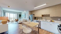 Located at 850 Pacific St in Stamford, Connecticut, this modern single-floor residence offers a thoughtfully designed open-concept layout that seamlessly connects the kitchen, dining, and living areas. The kitchen is well-appointed with stainless steel appliances — including a French door refrigerator, gas range, microwave, and dishwasher — complemented by two-tone cabinetry featuring light wood upper cabinets and crisp white lower cabinets, set against a neutral backsplash with ample counter space. A dining area with a light wood table and seating sits adjacent to the kitchen, making for an ideal everyday gathering space. The living area is bright and airy, with warm wood-style flooring flowing throughout, a media wall, and large sliding glass doors that open to a private balcony overlooking the Stamford cityscape. The bedroom is a calm retreat, featuring wood flooring, a floating wood shelf, and generous wall space. The bathroom offers a clean, modern aesthetic with a white vanity, large mirror, and well-lit fixtures. Throughout the residence, soft neutral tones, recessed and linear lighting, and contemporary finishes create a cohesive, inviting atmosphere ideal for modern urban living.