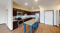 Located at 3000 N Chestnut St in Chaska, Minnesota, this single-floor residence offers a well-designed open-concept layout that seamlessly connects the kitchen, dining, and living areas. The kitchen is a standout feature, equipped with rich dark cabinetry, granite countertop surfaces, a central island with a contrasting navy-blue base, and a full suite of stainless steel appliances including a range, microwave, dishwasher, and refrigerator. Wood-style plank flooring extends throughout the main living areas, adding warmth and cohesion to the space.

The open living area is bright and generously sized, benefiting from natural light provided by large sliding glass doors that lead to a private balcony with exterior views. The bedrooms feature plush carpeting and ceiling fans, with one bedroom offering access to a walk-in closet with built-in shelving. The bathrooms are finished with granite-topped dark vanities, framed mirrors, and wood-style flooring. One bathroom includes a tub-shower combination, while another features an accessible walk-in shower layout. Overall, the space presents a clean, contemporary aesthetic with consistent, quality finishes throughout.