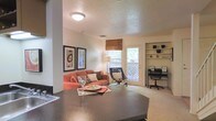This two-floor residence offers a well-designed layout that balances comfort and functionality. The main living area is open concept, seamlessly connecting the kitchen and living room for an airy, cohesive feel. The kitchen features a dark, textured countertop that serves as both a prep space and a casual dining surface, offering a clear sightline into the living area beyond.

The living room is warm and inviting, anchored by plush carpeting and a comfortable seating arrangement. A patio door with a woven roman shade allows generous natural light to filter in while providing access to the outdoors. Decorative framed artwork adorns the walls, adding a curated touch to the space.

A standout feature of the living area is the built-in shelving nook, which provides attractive display and storage space. Adjacent to it, a dedicated desk area with an ergonomic chair creates a practical home office alcove — ideal for work or study without occupying a separate room.

The textured ceiling and neutral wall tones throughout create a clean, timeless backdrop that complements a variety of décor styles. With two floors, the home offers separation between living and private spaces, providing both openness and privacy in a thoughtfully organized floor plan.