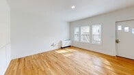 This single-floor unit at 211 Summer St in Buffalo's Elmwood Village neighborhood offers a thoughtfully designed layout comprising a living room, kitchen, and one bedroom. Warm, honey-toned hardwood floors extend throughout the entire space, creating a cohesive and inviting atmosphere.

The living room is bright and open, featuring large windows that invite natural light and classic wainscoting panels along the walls, adding a touch of architectural character. A recessed light fixture and a white radiator unit complete the space.

The kitchen is efficiently designed with a clean, modern aesthetic. White shaker-style cabinetry lines the walls from floor to ceiling, complemented by light quartz countertops, a white subway tile backsplash, and stainless steel appliances, including a range, microwave, and refrigerator.

The bedroom is a comfortable, well-proportioned room featuring multiple windows positioned near the ceiling, allowing natural light while maintaining privacy. Wainscoting panels mirror the living room's design, and a white radiator provides heating. Textured ceilings add subtle visual interest.

Throughout, the unit maintains a clean, freshly updated appearance with bright white walls and consistent finishes, creating a unified, modern living environment.