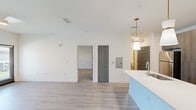 Located at Friends Crossing in Huntsville, Alabama, this thoughtfully designed one-bedroom, one-bathroom residence offers a clean, modern aesthetic throughout its single-floor layout. Light wood-look flooring flows through the main living areas, complemented by crisp white walls and bold six-panel doors in a contrasting dark finish that add character and definition to each space.

The open-concept kitchen and living area serves as the heart of the home. The kitchen is equipped with stainless steel appliances — including a refrigerator, electric range, and over-the-range microwave — set against a white subway tile backsplash. Rich, wood-toned cabinetry extends floor to ceiling, providing ample storage, while a large central island with a white quartz countertop and undermount sink doubles as a prep and gathering space. Dual pendant lights with gold hardware hang above the island, adding a warm, modern touch.

The living area is bright and airy, with natural light streaming through a window and glass-paneled entry door, further enhanced by a ceiling fan with an integrated light fixture.

The spacious bedroom features plush wall-to-wall carpeting, a ceiling fan, and generous proportions that offer comfortable flexibility in furnishing arrangements.

The bathroom is well-appointed with a double-sink vanity featuring dark wood cabinetry, white countertops, a large mirror, and a glass-enclosed shower with classic white subway tile.