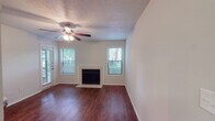 This single-floor residence offers a well-organized layout that balances comfort and functionality across its key living spaces. The living room serves as the heart of the home, showcasing rich, dark hardwood flooring, a classic wood-burning fireplace framed by a clean white surround, and multiple windows fitted with blinds that invite an abundance of natural light. A ceiling fan with an integrated light fixture keeps the space comfortable year-round, while the textured ceiling adds a traditional touch throughout.

The kitchen is efficiently designed in a galley-style configuration, featuring white cabinetry with brushed nickel hardware, granite-look countertops, a subway tile backsplash, and black appliances including a range and dishwasher. Dark hardwood flooring continues from the living area into the kitchen, maintaining visual continuity.

The bedroom is generously proportioned, with soft carpeting underfoot, a ceiling fan, textured ceiling, and a full-width sliding glass door with vertical blinds that opens to an outdoor patio, providing pleasant views of surrounding greenery.

The bathroom is clean and functional, offering a full-size soaking tub with an overhead shower, tiled surround in classic white, and brushed nickel fixtures that complement the overall neutral palette of the space.