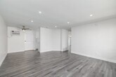 Located in Downey, CA, this thoughtfully designed 2-bedroom, 2-bathroom unit offers a clean, modern aesthetic across its single floor. Light gray wood-look flooring flows consistently throughout every room, complementing the crisp white walls and bright, open atmosphere.

The spacious living room features recessed lighting and a large window that invites natural light and outdoor views, creating an airy and welcoming environment. A dedicated entry door adds convenience and privacy.

The kitchen is outfitted with white shaker cabinetry, brushed nickel hardware, white quartz countertops, a subtle penny-tile backsplash, and stainless steel appliances including a full-size refrigerator and dishwasher — a functional and stylish space for everyday cooking.

Both bedrooms are well-sized, with the primary bedroom offering comfortable proportions, a ceiling fan with a brushed gold fixture, and a wall-mounted AC unit for climate control. The second bedroom also includes a ceiling fan and a bright window with neighborhood views.

The two bathrooms are finished in clean, modern white. One features a glass-enclosed walk-in shower with brushed nickel fixtures, while the other offers a full tub-shower combination with a white vanity and large mirror. Together, they provide practical and polished functionality throughout this move-in ready home.