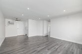 Located in Downey, CA, this thoughtfully designed 2-bedroom, 2-bathroom unit offers a clean, modern aesthetic across its single floor. Light gray wood-look flooring flows consistently throughout every room, complementing the crisp white walls and bright, open atmosphere.

The spacious living room features recessed lighting and a large window that invites natural light and outdoor views, creating an airy and welcoming environment. A dedicated entry door adds convenience and privacy.

The kitchen is outfitted with white shaker cabinetry, brushed nickel hardware, white quartz countertops, a subtle penny-tile backsplash, and stainless steel appliances including a full-size refrigerator and dishwasher — a functional and stylish space for everyday cooking.

Both bedrooms are well-sized, with the primary bedroom offering comfortable proportions, a ceiling fan with a brushed gold fixture, and a wall-mounted AC unit for climate control. The second bedroom also includes a ceiling fan and a bright window with neighborhood views.

The two bathrooms are finished in clean, modern white. One features a glass-enclosed walk-in shower with brushed nickel fixtures, while the other offers a full tub-shower combination with a white vanity and large mirror. Together, they provide practical and polished functionality throughout this move-in ready home.