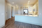 This single-floor residence at 402 Highway 23 NW in Suwanee, Georgia, offers a clean, modern aesthetic defined by consistent design choices throughout. Dark hardwood-style flooring flows seamlessly across the living areas and bedrooms, providing a warm contrast to the neutral gray and white walls that characterize every room.

The kitchen serves as a central highlight, featuring an expansive island with a quartz countertop and a deep stainless steel sink fitted with a professional-style faucet. Upper cabinetry combines crisp white panels with glass-front accents, while lower cabinets are finished in a warm gray tone. Stainless steel appliances, including a refrigerator with French doors, a range, and a built-in microwave, complete the well-appointed space. Pendant lighting above the island and recessed ceiling lights provide layered illumination throughout.

The bedroom areas offer a calm, open atmosphere, with one room featuring a ceiling fan and a window that brings in natural light. Hallways connect the living spaces to additional rooms, with multiple doors providing access to closets and secondary spaces.

The bathroom is finished with a wide vanity topped in speckled quartz, gray cabinetry with brushed nickel hardware, an undermount sink, and a large frameless mirror. The overall ambiance throughout is contemporary, light, and well-maintained.
