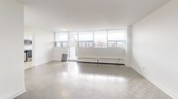 Located at Fowler Drive in Mississauga, this one-bedroom, one-bathroom unit offers a well-organized layout across a single floor. The bright white walls and light-toned parquet flooring create a clean, modern aesthetic throughout the space.

The living room is a standout, featuring a wide band of floor-to-ceiling windows that flood the room with natural light and frame panoramic views of the surrounding Mississauga cityscape. Baseboard heating runs beneath the windows, and the open feel of the room provides excellent versatility for furniture arrangement.

The kitchen is thoughtfully appointed with stainless steel appliances, including a range and over-the-range microwave, complemented by white cabinetry and a herringbone-patterned tile backsplash. Light-toned floor tiles and a window overlooking the city make the kitchen feel airy and functional.

The bedroom is a comfortable, well-proportioned room with the same consistent white walls and parquet flooring, offering a calm and quiet retreat.

The bathroom features crisp white subway tile surrounding the soaker tub and shower, paired with large-format stone-look floor tiles, a floating vanity with a white countertop, and a large mirror — a clean, contemporary finish throughout.

Overall, the unit offers a bright, minimalist atmosphere with consistent finishes and sweeping urban views.