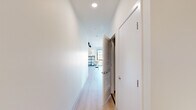 This thoughtfully designed one-bedroom, one-bathroom unit offers an efficient and modern living experience across a single floor. Light-toned hardwood flooring runs throughout, creating a clean, cohesive aesthetic that ties every room together.

The open-concept living and dining area is a standout feature, anchored by floor-to-ceiling grid-style windows with black frames that flood the space with natural light and frame elevated views of the surrounding cityscape. The dining area comfortably accommodates a round table and chairs, while the living room provides ample space for a sectional sofa and features a wall-mounted mini-split system for climate control.

The galley kitchen is well-appointed with light wood cabinetry extending to the ceiling, white quartz countertops, a white subway tile backsplash, and a full suite of stainless steel appliances including a refrigerator, range, and built-in microwave. Track lighting overhead adds both function and a contemporary touch.

A bright hallway connects the living areas to the private bedroom, which includes a ceiling fan, a mini-split unit, and a large grid window with city rooftop views. A dedicated closet provides organized storage.

The bathroom features light wood vanity cabinetry, white quartz counters, a tiled tub-shower combination, and light wood-look flooring, completing the unit's clean, modern design language.