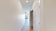 This thoughtfully designed one-bedroom, one-bathroom unit offers an efficient and modern living experience across a single floor. Light-toned hardwood flooring runs throughout, creating a clean, cohesive aesthetic that ties every room together.

The open-concept living and dining area is a standout feature, anchored by floor-to-ceiling grid-style windows with black frames that flood the space with natural light and frame elevated views of the surrounding cityscape. The dining area comfortably accommodates a round table and chairs, while the living room provides ample space for a sectional sofa and features a wall-mounted mini-split system for climate control.

The galley kitchen is well-appointed with light wood cabinetry extending to the ceiling, white quartz countertops, a white subway tile backsplash, and a full suite of stainless steel appliances including a refrigerator, range, and built-in microwave. Track lighting overhead adds both function and a contemporary touch.

A bright hallway connects the living areas to the private bedroom, which includes a ceiling fan, a mini-split unit, and a large grid window with city rooftop views. A dedicated closet provides organized storage.

The bathroom features light wood vanity cabinetry, white quartz counters, a tiled tub-shower combination, and light wood-look flooring, completing the unit's clean, modern design language.