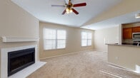 Located at 5450 Firewater Ln. in Columbus, Ohio, this single-floor home offers a well-designed, open layout with a warm and neutral palette throughout. The expansive living room is a centerpiece of the home, highlighted by vaulted ceilings, a ceiling fan with light fixture, and a tiled fireplace with a clean white mantel. Multiple windows dressed with horizontal blinds fill the space with natural light, creating a bright and welcoming atmosphere. Plush wall-to-wall carpeting extends throughout the living areas and bedrooms, adding comfort underfoot.

The kitchen is efficiently laid out with warm wood cabinetry, stainless steel appliances including a refrigerator, range, and microwave, as well as a double sink set into a countertop that opens to a breakfast bar, allowing easy interaction with the adjoining living space. Wood-look flooring grounds the kitchen for easy maintenance.

Additional rooms include generously sized carpeted bedrooms, one of which features a sliding glass door leading to an outdoor patio area. A built-in shelving nook adds a functional design detail. The bathroom is equipped with a vanity featuring wood cabinetry, wood-look tile flooring, and a full tub-shower combination. A dedicated laundry alcove with utility connections completes this practical and comfortable home.