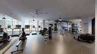Located at 4520 Charlotte Park Dr in Charlotte, NC, this expansive single-floor fitness center offers a comprehensive workout environment designed to support a wide range of exercise disciplines. The space is thoughtfully organized into distinct training zones, each outfitted with professional-grade equipment.

The cardio zone lines the windowed perimeter, where large floor-to-ceiling windows invite abundant natural light and views of the surrounding exterior. True-brand treadmills, ellipticals, rowing machines, and a stair climber are neatly arranged in this bright area, enhanced by ceiling fans that promote airflow throughout.

At the heart of the facility, a multi-functional cable machine and a robust overhead rig with pull-up bars support strength and functional training. A dedicated free weights area includes a full rack of dumbbells, barbells, and benches. Pendant lighting fixtures complement the modern, neutral-toned interior.

A standout feature of the space is its functional training zone, which includes a large tire flip station and battle ropes for high-intensity workouts. A colorful bouldering wall anchors one end of the room, adding a unique and engaging element rarely found in residential fitness centers. Vibrant wall murals add artistic energy to the space. Durable rubberized flooring runs throughout, ensuring safety and comfort across all training activities.
