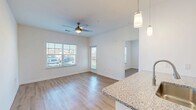 This single-floor, one-bedroom, one-bathroom unit in Foley, Alabama offers a thoughtfully designed open-concept layout that maximizes its efficient footprint. The combined kitchen and living area serves as the heart of the home, featuring warm wood-look flooring that extends throughout the space, crisp white walls, and a ceiling fan that enhances air circulation and comfort. Large windows flood the living area with abundant natural light while providing outdoor views, and a private exterior door adds convenient access. The kitchen is well-appointed with white shaker-style cabinetry, granite countertops, stainless steel appliances including a refrigerator, range, and microwave, and a peninsula with a sink that doubles as a casual dining or prep area. Stylish pendant lighting accents the kitchen peninsula. The bedroom is a comfortable, well-lit retreat with a ceiling fan, a generously sized window, and access to a dedicated closet. The bathroom continues the clean aesthetic with a white vanity, granite countertop, undermount sink, brushed nickel fixtures, a large mirror, and matching wood-look flooring. The overall design is clean, modern, and cohesive, making this Foley unit a practical and attractive living space.