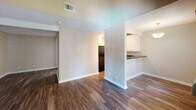 Located at 1919 E Birch St in Brea, California, this single-floor unit offers a thoughtfully designed layout with a cohesive, neutral color palette throughout. Dark hardwood-style flooring flows seamlessly across the main living areas, complementing the warm beige and taupe tones of the walls and crisp white baseboards.

The living area is a standout, featuring striking vaulted ceilings with exposed white wooden beams that add architectural character and a sense of openness. A sliding glass door floods the space with natural light and opens to a private balcony with views of the surrounding landscape. A wall-mounted HVAC unit ensures year-round comfort.

The kitchen is well-appointed with rich dark granite countertops, white raised-panel cabinetry offering generous storage, a stainless steel sink, and black appliances including a dishwasher and range. A pass-through counter connects the kitchen to the adjacent living and dining areas, creating an open, functional flow.

The bedroom features a textured ceiling, a sliding mirrored closet, and the same dark hardwood-style flooring found throughout the unit. The bathroom includes white cabinetry with granite countertops, a single vanity with dual mirrors, and a full tub-shower combination, finished with wood-look flooring for a cohesive aesthetic.