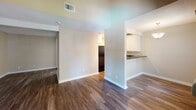 Located at 1919 E Birch St in Brea, California, this single-floor unit offers a thoughtfully designed layout with a cohesive, neutral color palette throughout. Dark hardwood-style flooring flows seamlessly across the main living areas, complementing the warm beige and taupe tones of the walls and crisp white baseboards.

The living area is a standout, featuring striking vaulted ceilings with exposed white wooden beams that add architectural character and a sense of openness. A sliding glass door floods the space with natural light and opens to a private balcony with views of the surrounding landscape. A wall-mounted HVAC unit ensures year-round comfort.

The kitchen is well-appointed with rich dark granite countertops, white raised-panel cabinetry offering generous storage, a stainless steel sink, and black appliances including a dishwasher and range. A pass-through counter connects the kitchen to the adjacent living and dining areas, creating an open, functional flow.

The bedroom features a textured ceiling, a sliding mirrored closet, and the same dark hardwood-style flooring found throughout the unit. The bathroom includes white cabinetry with granite countertops, a single vanity with dual mirrors, and a full tub-shower combination, finished with wood-look flooring for a cohesive aesthetic.