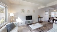 This two-floor residence offers a thoughtfully designed layout with two bedrooms and one and a half bathrooms, blending modern finishes with a clean, minimalist aesthetic. Light wood-style flooring runs consistently throughout the home, contributing to a cohesive and airy feel.

The living area on the main floor features exposed beam ceilings with white shiplap detailing, adding architectural character to the space. Natural light filters in through windows, brightening the open area that flows toward the kitchen. The galley-style kitchen is equipped with stainless steel appliances, dark countertops, white cabinetry, and a stacked washer and dryer unit conveniently integrated into the layout. A half bathroom is also accessible on the main floor.

Both bedrooms are located upstairs and share a bright, neutral palette with white walls and ceiling fans. Each room features sleek mirrored sliding closet doors with black frames, offering ample storage. Windows in each bedroom invite natural light and outdoor views. The full bathroom includes a tub-shower combination with white subway tile, a single vanity, and a frosted window for privacy.

Overall, the space presents a modern, well-organized design with practical amenities distributed efficiently across both floors.