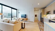 Located on W Eastman St in Chicago's vibrant 60642 corridor, this modern single-floor residence is defined by clean lines, warm natural materials, and sweeping city views. The open-concept living and dining area is anchored by expansive floor-to-ceiling windows with sleek black frames, flooding the space with natural light and offering striking panoramic views of the Chicago skyline. Light-toned hardwood flooring runs throughout, lending warmth and continuity to every room. The living area comfortably accommodates a sectional sofa, a low-profile media console in natural wood, and a round coffee table, creating an inviting and well-appointed gathering space. The kitchen is outfitted with light wood cabinetry extending to the ceiling, a white herringbone tile backsplash, white quartz countertops, and a full suite of stainless steel appliances including a gas range and French door refrigerator. The bedroom benefits from its own set of floor-to-ceiling windows framing city views, a built-in closet, and light hardwood floors. The bathroom features a wood-toned vanity with white countertop, light tile flooring, and a clean, minimalist aesthetic. This residence masterfully blends contemporary design with functional urban living.