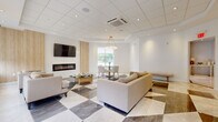 Located at 507 E Main St in Bound Brook, NJ, this single-floor space showcases a refined, contemporary design with high-end finishes throughout. The main lounge area is a standout, featuring a striking geometric marble-tile floor in contrasting light and dark tones, a sleek linear electric fireplace set against a warm wood-panel accent wall, and a wall-mounted flat-screen television. Plush neutral-toned seating arrangements create an inviting, comfortable atmosphere, while a round glass coffee table adds a touch of sophistication. A dedicated dining nook is anchored by a round glass-top table with gold-accented legs, surrounded by elegant upholstered chairs and illuminated by a striking circular crystal chandelier. Natural light fills the space through multiple large windows dressed with clean roller shades, complemented by gold wall sconces that add a warm, ambient glow. The kitchenette area is outfitted with crisp white shaker cabinetry, white quartz countertops, a subway tile backsplash, a stainless steel sink, and an under-counter beverage refrigerator. Additional cabinetry and prep space provide generous storage and utility. The overall ambiance is bright, airy, and polished, making this a versatile and visually impressive space.