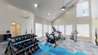 Located at 22900 Oak Ridge Dr in Santa Clarita, CA, this well-appointed fitness center offers a comprehensive workout environment within a single-floor layout. The space is immediately distinguished by its soaring vaulted ceilings, which create an open and energizing atmosphere enhanced by recessed lighting and ceiling fans that keep the room well-ventilated and comfortable during workouts.

The fitness center is equipped with a thoughtful selection of exercise equipment, including a treadmill, elliptical trainer, stationary cycle, and a stair climber, providing a full range of cardio options. A multi-tiered dumbbell rack lines one wall alongside a large wall mirror, ideal for strength training and monitoring form. TRX suspension training straps are wall-mounted, offering functional fitness versatility, while kettlebells and medicine balls round out the free-weight offerings.

Natural light filters in through frosted windows along multiple walls, maintaining privacy while keeping the space bright. A dedicated entry area with double glass doors connects the fitness center to an adjacent common lounge area, improving overall accessibility and flow. The striking geometric-patterned flooring in shades of blue, grey, and teal adds a modern, dynamic visual element to the space, complementing the clean, neutral-toned walls throughout.