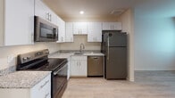Located at 1012 Shiloh Way in Morrisville, NC, this single-floor unit offers a thoughtfully designed layout with a clean, contemporary aesthetic carried consistently throughout the space. Light-toned wood-look flooring flows seamlessly from room to room, creating a cohesive and bright atmosphere.

The kitchen is a standout feature, showcasing white shaker-style cabinetry with sleek hardware, granite-look countertops, a tile backsplash, and a full suite of stainless steel GE appliances — including a refrigerator, electric range, over-the-range microwave, and dishwasher. Recessed lighting illuminates the space effectively, and an adjacent entry door provides direct access to the exterior.

The living area is open and versatile, benefiting from the continuity of flooring and neutral wall tones that lend a bright, welcoming feel. A bedroom offers a window with natural light, neutral walls, and ample room for furnishings, with a wall-mounted panel adding a practical touch.

The bathroom is well-appointed with white cabinetry, a granite-look vanity countertop with an undermount sink, a walk-in shower with sliding glass doors, and a toilet — all finished with the same light flooring found throughout. Conveniently adjacent to the bathroom, a stacked GE washer and dryer unit provides in-unit laundry, maximizing both functionality and use of space.