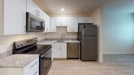 Located at 1012 Shiloh Way in Morrisville, NC, this single-floor unit offers a thoughtfully designed layout with a clean, contemporary aesthetic carried consistently throughout the space. Light-toned wood-look flooring flows seamlessly from room to room, creating a cohesive and bright atmosphere.

The kitchen is a standout feature, showcasing white shaker-style cabinetry with sleek hardware, granite-look countertops, a tile backsplash, and a full suite of stainless steel GE appliances — including a refrigerator, electric range, over-the-range microwave, and dishwasher. Recessed lighting illuminates the space effectively, and an adjacent entry door provides direct access to the exterior.

The living area is open and versatile, benefiting from the continuity of flooring and neutral wall tones that lend a bright, welcoming feel. A bedroom offers a window with natural light, neutral walls, and ample room for furnishings, with a wall-mounted panel adding a practical touch.

The bathroom is well-appointed with white cabinetry, a granite-look vanity countertop with an undermount sink, a walk-in shower with sliding glass doors, and a toilet — all finished with the same light flooring found throughout. Conveniently adjacent to the bathroom, a stacked GE washer and dryer unit provides in-unit laundry, maximizing both functionality and use of space.