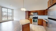 This single-floor residence offers a thoughtfully designed layout that maximizes functionality across a generous footprint. The open-concept kitchen and living area serves as the heart of the home, featuring rich warm-toned wood cabinetry, stainless steel appliances, a subway tile backsplash, and a granite-topped kitchen island with pendant lighting overhead. The kitchen transitions seamlessly into the living area, which is finished with durable hardwood-style flooring and benefits from natural light through large windows.

The bedroom is a comfortable, carpeted retreat featuring an interior transom window above the door that allows light to flow between spaces. A walk-in closet with wire shelving provides ample storage. The five bathrooms offer variety in fixtures, including a full tub-and-shower combination with a framed vanity mirror and granite countertop, as well as a standalone walk-in shower.

A dedicated office or flex space features exposed industrial ductwork along the ceiling, adding a modern urban character, along with a built-in wood desk and cabinetry. The in-unit laundry room houses a full-size side-by-side washer and dryer with overhead wire shelving. The combination of modern finishes, industrial accents, and practical amenities makes this a versatile and functional living space.