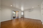 This single-floor residence offers a clean, bright interior with a cohesive design throughout. The living area features warm wood-look flooring, recessed lighting, and crown molding, lending a polished feel to the open layout. A sliding glass door connects the living space to a private balcony enclosed with decorative ironwork railings, offering pleasant outdoor views of the surrounding neighborhood.

The galley-style kitchen is well-equipped with rich cherry wood cabinetry, granite-look countertops, and a full suite of stainless steel appliances including a gas range, microwave, refrigerator, and dishwasher. Tile flooring runs through the kitchen, complementing the warm tones of the cabinetry.

The residence includes multiple bedrooms, each finished with wood-look flooring, crown molding, and ceiling fans. Several rooms feature mirrored sliding closet doors for added storage. At least one bedroom is equipped with a wall-mounted mini-split air conditioning unit for individual climate control. Natural light flows generously through vertical-blind-covered windows in each room.

The bathroom features a rich wood vanity with a granite-look countertop, a single sink, and a full tub-shower combination with clean white tile surround. Throughout the home, the neutral color palette and consistent finishes create a bright, inviting, and move-in ready atmosphere.