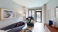 Located at 240 Park Ave in the heart of Minneapolis, this thoughtfully designed single-floor residence offers a refined urban living experience. The open-concept layout is anchored by a sleek, modern kitchen outfitted with white shaker cabinetry extending to the ceiling, granite-style countertops, a subway tile backsplash, stainless steel appliances including a gas range, dishwasher, and refrigerator, and a generous island that provides additional prep and dining space. Light hardwood flooring flows throughout the main living areas, lending warmth and continuity to the space. The living area features floor-to-ceiling windows with black-framed doors opening to a balcony, flooding the room with natural light and offering views of the surrounding Minneapolis streetscape. A dedicated workspace area sits neatly within the living room, making the space as functional as it is inviting. The bedroom is carpeted for comfort, equipped with a ceiling fan, and boasts expansive windows that frame vivid city views. The full bathroom is finished with a wood-framed vanity mirror, granite countertops, white cabinetry, and a tiled shower-tub combination. Throughout the residence, a neutral, contemporary palette and curated furnishings create a calm, sophisticated ambiance well-suited to urban living.