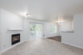 This single-floor residence offers a thoughtfully designed layout that balances comfort and functionality throughout its living spaces. The spacious living room serves as a central gathering area, highlighted by a built-in fireplace with a clean white mantel and sliding glass doors fitted with vertical blinds that provide access to an outdoor patio. Neutral-toned carpet flows throughout the living and bedroom areas, lending a warm and cohesive feel to the space.

Adjacent to the living room, the dining area features wood-look flooring, a chandelier overhead, a bright window framing greenery outside, and direct access to a second patio door. The kitchen is efficiently designed with white cabinetry, a subway tile backsplash, dark countertops, stainless steel appliances including a range and refrigerator, and a peninsula that opens toward the dining area.

The bedrooms are carpeted and well-lit by natural light from windows overlooking outdoor greenery, with baseboard heating providing comfort. Bathrooms include a full bath with a soaking tub and tile flooring, and a second bath featuring a glass-enclosed shower and wood-look flooring. Throughout the residence, neutral walls and clean finishes create a bright, move-in-ready atmosphere.