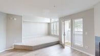 Located at 10 Gentrys Walk in Atlanta, Georgia, this single-floor residence offers a thoughtfully designed layout with a clean, contemporary aesthetic throughout. The living area is a standout space, featuring soaring vaulted ceilings and a striking arched window that floods the room with abundant natural light. Light hardwood-style flooring extends across the main living spaces, while plush carpeting defines the recessed bedroom platform area. A fireplace with a sleek black surround anchors one wall of the living room, and direct access to an outdoor balcony brings in additional light and views of the surrounding greenery.

The kitchen is well-appointed with white shaker cabinetry, contrasting gray lower cabinets, a herringbone tile backsplash, stainless steel appliances including a gas range, microwave, and refrigerator, and a central island with a white countertop that provides additional prep and dining space. Light hardwood floors continue throughout the kitchen for a cohesive feel.

The bathroom includes both a soaking tub and a separate glass-enclosed shower, finished with light flooring and neutral wall tones. A spacious walk-in closet with built-in wire shelving and hardwood flooring provides generous storage. The overall palette of soft grays, whites, and warm wood tones creates a bright, clean, and inviting atmosphere throughout the home.