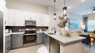 This well-appointed one-bedroom, one-bathroom residence offers a smart, efficient single-floor layout with modern finishes throughout. The open-concept kitchen and living area serves as the heart of the home, featuring two-toned cabinetry — crisp white upper cabinets paired with grey lower cabinets — complemented by a dark subway tile backsplash and sleek quartz countertops. A peninsula with seating for two anchors the space, illuminated by stylish pendant lighting. Stainless steel appliances complete the kitchen. The adjoining living area is bright and inviting, with large windows that allow natural light to pour in, light wood-style flooring, and a ceiling fan overhead. The bedroom is a calm retreat with multiple windows, ample natural light, and direct access to the full bathroom. The bathroom features grey cabinetry with matte black hardware, a quartz-topped vanity, and a glass-enclosed walk-in shower. A generously sized walk-in closet with multi-level shelving and hanging rods provides practical storage. Neutral warm tones and consistent wood-style flooring tie the entire space together, creating a cohesive and welcoming atmosphere throughout.