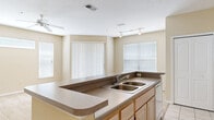Located at 5819 Legacy Crescent Pl in Riverview, FL, this single-story home offers a practical, open layout with a neutral color palette throughout. The kitchen serves as a central feature of the space, equipped with light wood cabinetry, dark countertops, a double-basin sink set into a peninsula, and white appliances including an electric range and refrigerator. Track lighting illuminates the kitchen area, while a window allows natural light to filter in. The peninsula connects the kitchen to the adjacent living area, which features warm-toned carpet and multiple windows fitted with horizontal and vertical blinds, enhancing natural light across the open floor plan. A ceiling fan adds to the comfort of the living space.

The bedrooms continue the carpeted flooring and maintain the home's neutral beige tones, each featuring windows with blinds that bring in outdoor views. The bathroom is finished with light tile flooring, a white vanity with storage cabinetry, a wall-mounted mirror, and a tiled tub and shower combination. Overall, the home presents a clean, functional interior well-suited to comfortable everyday living in the Riverview community.