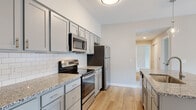 Located at 311 W Johnstown Rd in Gahanna, Ohio, this single-floor residence offers a well-designed, contemporary living space with thoughtful finishes throughout. The open-concept kitchen serves as the centerpiece of the home, showcasing a granite countertop island with a stainless steel sink and elegant pendant lighting. Gray shaker-style cabinetry lines the kitchen walls, complemented by a classic white subway tile backsplash and a full suite of stainless steel appliances, including a refrigerator, range, and microwave. Warm-toned hardwood-style flooring flows throughout the kitchen and main living areas, creating a cohesive and inviting atmosphere. The living area transitions seamlessly from the kitchen, providing an open and versatile layout. The bedrooms are carpeted for comfort and each feature ample closet space and windows that allow natural light to brighten the rooms. Two bathrooms serve the home — one featuring a distinctive blue vanity with a white countertop and a walk-in shower, and the other with a gray vanity, white countertop, and a bathtub. Both bathrooms are finished with hardwood-style flooring and well-lit vanity mirrors. Overall, the space presents a clean, modern aesthetic with neutral tones and quality finishes throughout.