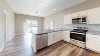 Located at 320 W 3rd St N in Newton, Iowa, this 2-bedroom, 2-bathroom unit offers a well-planned single-floor layout designed for comfortable everyday living. The kitchen serves as a central highlight, featuring white shaker cabinetry, granite-style countertops, a peninsula with an undermount sink, and a full suite of stainless steel appliances including a gas range, microwave, dishwasher, and refrigerator. Wood-style plank flooring runs throughout the kitchen and living areas, providing a clean, modern aesthetic, while the bedrooms are finished with plush carpet for added comfort. Natural light flows into the living area through a sliding glass door and windows offering views of the surrounding neighborhood. The primary bathroom is outfitted with a wide vanity featuring white cabinetry and a large mirror, wood-style flooring, and direct access to a spacious walk-in closet with wire shelving on multiple walls. The second bathroom includes a full tub-shower combination. A dedicated in-unit laundry closet houses a full-size washer and dryer. On-site parking is available, with views of downtown Newton visible from the property. The unit presents a clean, modern interior with neutral tones throughout.
