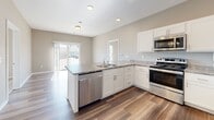 Located at 320 W 3rd St N in Newton, Iowa, this 2-bedroom, 2-bathroom unit offers a well-planned single-floor layout designed for comfortable everyday living. The kitchen serves as a central highlight, featuring white shaker cabinetry, granite-style countertops, a peninsula with an undermount sink, and a full suite of stainless steel appliances including a gas range, microwave, dishwasher, and refrigerator. Wood-style plank flooring runs throughout the kitchen and living areas, providing a clean, modern aesthetic, while the bedrooms are finished with plush carpet for added comfort. Natural light flows into the living area through a sliding glass door and windows offering views of the surrounding neighborhood. The primary bathroom is outfitted with a wide vanity featuring white cabinetry and a large mirror, wood-style flooring, and direct access to a spacious walk-in closet with wire shelving on multiple walls. The second bathroom includes a full tub-shower combination. A dedicated in-unit laundry closet houses a full-size washer and dryer. On-site parking is available, with views of downtown Newton visible from the property. The unit presents a clean, modern interior with neutral tones throughout.
