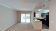 This 1-bedroom, 1-bathroom apartment is thoughtfully designed to maximize comfort and functionality across a single floor. The open-concept living and dining area is anchored by a decorative column and elegant crown molding, lending a refined architectural touch. Plush carpeting flows throughout the main living spaces, while a sliding glass door floods the room with natural light and provides direct access to a private balcony overlooking lush greenery.

The kitchen is efficiently laid out with dark cabinetry, granite-style countertops, and a breakfast bar that seamlessly connects to the living area — ideal for casual dining or entertaining. Dark hardwood-style flooring grounds the kitchen and extends into the bathroom, creating a cohesive contrast with the lighter tones throughout.

The bathroom features a granite-topped vanity with a single sink, dark wood cabinetry, a full tub-shower combo, and ample lighting provided by a Hollywood-style vanity fixture. The bedroom is complemented by a generously sized walk-in closet, outfitted with multi-level wire shelving for organized storage. Textured ceilings and neutral warm-beige walls throughout create a welcoming, move-in-ready atmosphere.