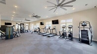Located in Knoxville, Tennessee, this fitness center at 13300 Ardmore Valley Way is a thoughtfully designed exercise facility that offers a comprehensive workout experience across a generously sized single floor. The space is divided into distinct functional zones, each purpose-built to support a wide range of training styles.

The cardio area features a row of treadmills, a stationary bike, a rowing machine, and an elliptical, all positioned along a wall of windows that allow abundant natural light and views of the surrounding community. Dual flat-screen TVs are mounted overhead, and large ceiling fans help maintain a comfortable environment throughout.

Adjacent to the cardio zone, the strength and functional training area is anchored by a multi-station cable machine, a full rack of dumbbells, a power rack with a barbell bench, and a selection of weight plates and kettlebells. A wall-mounted mirror expands the sense of space and supports proper form during workouts.

A vibrant functional training turf zone, distinguished by bold geometric wall art in blue, yellow, and teal, features a climbing wall, a boxing/striking station, and additional specialty equipment. The turf surface provides an ideal area for dynamic movements and group training.

The facility also includes a tiled entry corridor with large glass double doors, a well-appointed restroom or changing area with stone accent walls, and recessed lighting throughout. The clean, modern design and diverse equipment selection make this a highly functional and welcoming fitness facility.