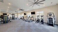 Located in Knoxville, Tennessee, this fitness center at 13300 Ardmore Valley Way is a thoughtfully designed exercise facility that offers a comprehensive workout experience across a generously sized single floor. The space is divided into distinct functional zones, each purpose-built to support a wide range of training styles.

The cardio area features a row of treadmills, a stationary bike, a rowing machine, and an elliptical, all positioned along a wall of windows that allow abundant natural light and views of the surrounding community. Dual flat-screen TVs are mounted overhead, and large ceiling fans help maintain a comfortable environment throughout.

Adjacent to the cardio zone, the strength and functional training area is anchored by a multi-station cable machine, a full rack of dumbbells, a power rack with a barbell bench, and a selection of weight plates and kettlebells. A wall-mounted mirror expands the sense of space and supports proper form during workouts.

A vibrant functional training turf zone, distinguished by bold geometric wall art in blue, yellow, and teal, features a climbing wall, a boxing/striking station, and additional specialty equipment. The turf surface provides an ideal area for dynamic movements and group training.

The facility also includes a tiled entry corridor with large glass double doors, a well-appointed restroom or changing area with stone accent walls, and recessed lighting throughout. The clean, modern design and diverse equipment selection make this a highly functional and welcoming fitness facility.